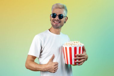 Çekici hipster adam elinde patlamış mısırla renkli bir arka plan tutuyor.