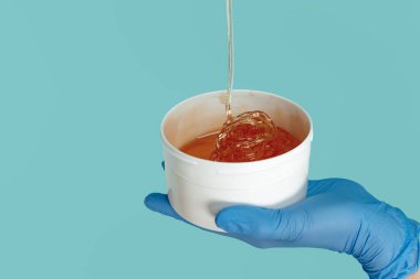 Mavi arkaplan üzerinde tüy dökme işlemi için şekerli kovayı tutan eller