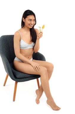 Olumlu Asyalı genç bir kadın ustura tutuyor ve tüy dökmek için makarnaya yapışıyor..