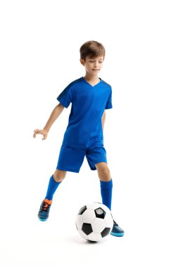 Mavi spor kıyafetli genç, beyaz arka planda klasik futbol topuyla oynuyor..
