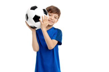 Mavi spor kıyafetli komik çocuk beyaz arka planda klasik futbol topuyla poz veriyor..