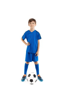 Sevimli genç futbolcu, mavi spor kıyafetli klasik futbol topunun bacağını tutuyor..