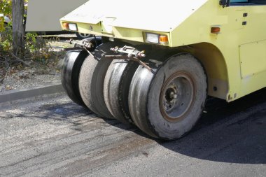 Yol titreşimli silindirler, şehrin arka planındaki yol inşaatında güçlü bir şekilde taze asfaltı sıkıştırır..