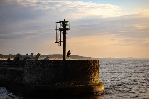 Gün batımında Ustka 'daki rıhtımda balık tutan bir balıkçı.