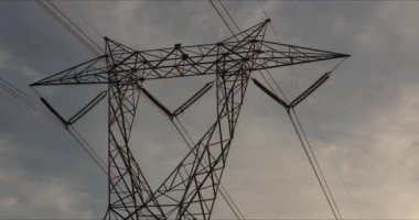 Timelapse video of clouds passing by electric transmission tower at dusk.