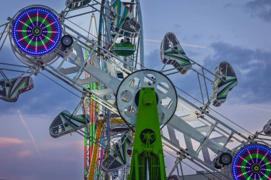 Uzun mercekli yakın plan, alacakaranlık gökyüzüne karşı kurulmuş karnaval araçlarının çelik ve makinelerini gösteriyor..