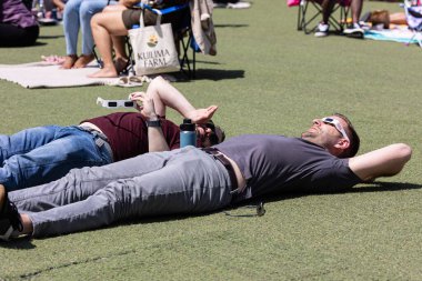 Atlanta, GA / ABD - 8 Nisan 2024: İki erkek, 8 Nisan 2024 'te Atlanta, GA' da düzenlenen bir saat partisinde güneş tutulmasını izlemek için yerde yatıp özel gözlüklerden bakıyor.