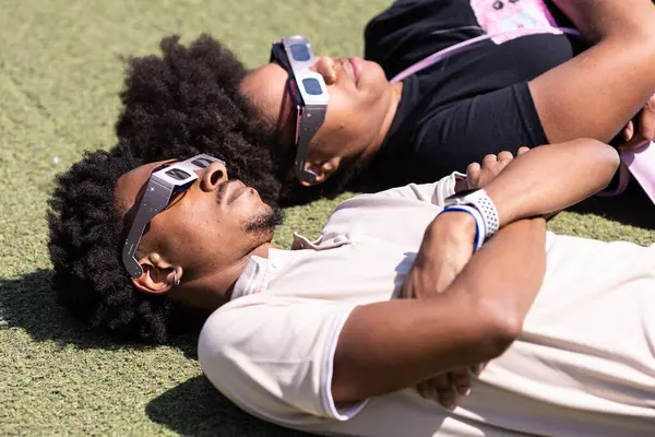 美国亚特兰大 2024年4月8日 一对夫妇戴着特制的眼镜躺在地上观看2024年4月8日在美国亚特兰大举行的一个手表派对上的日全食 免版税图库照片