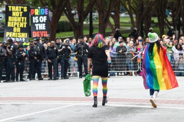 Atlanta, GA / USA - 15 Ekim 2023: Gururlu renkler giyen iki kadın 15 Ekim 2023 'te Atlanta, GA' da düzenlenen yıllık gurur yürüyüşünde sağcı homofobik işaretlerin yanından geçtiler..
