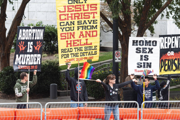 Atlanta, GA / USA - October 15, 2023:  A woman defiantly waves pride flags directly in front of anti-gay activists holding homophobic signs on October 15, 2023 in Atlanta, GA.