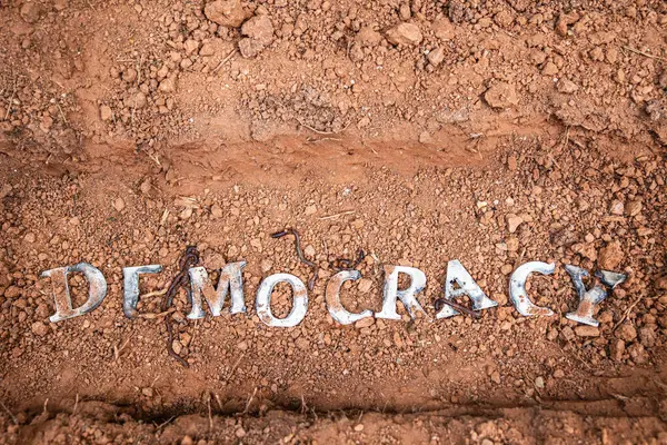 stock image Wood letters that spell out the word democracy, lie in a shallow grave, suggesting democracy is being buried.