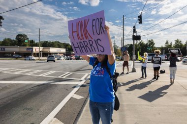 Lawrenceville, GA / USA - September 5, 2024:  Democratic party activists hold campaign signs promoting Kamala Harris in a local Honk for Kamala Harris event at a busy street corner, on September 5, 2024 in Lawrenceville, GA. clipart