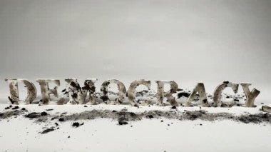 Statik çekim, beyaz, pürüzsüz bir zeminde oturan demokrasi sözcüğünü heceleyen kömürleşmiş ahşap harfleri gösteriyor. Demokrasi saldırı altında.. 