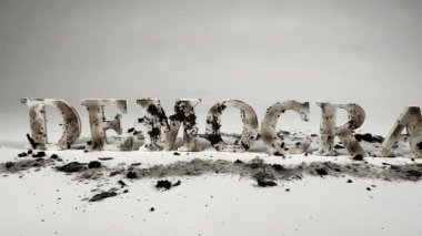 Yavaş çekim, kömürleşmiş ahşap harfleri gösteriyor. Demokrasi kelimesini heceliyor, küllerin arasında beyaz, pürüzsüz bir arkaplan karşısında oturuyor. Demokrasinin saldırı altında olduğunu gösteriyor.. 