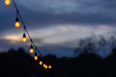 Verandaya asılmış bir dizi parlak Edison ampulü mor bir alacakaranlık gökyüzüne karşı neşeli bir parti havası yaratıyor..