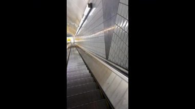 Yavaş çekim, tren istasyonu tünelinde aşağı doğru ilerleyen çok uzun bir yürüyen merdivenin adımlarını gösteriyor.. 