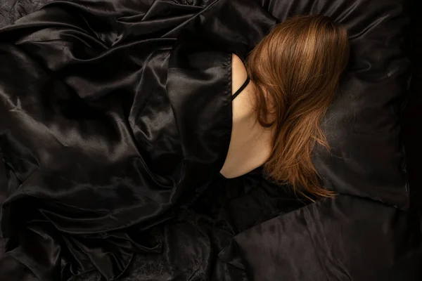 Woman sleeps in a bed on black bed sheet. Sleeping concept.