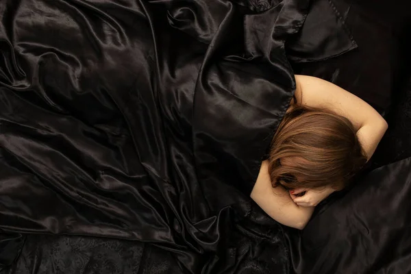 Woman sleeps in a bed on black bed sheet. Sleeping concept.