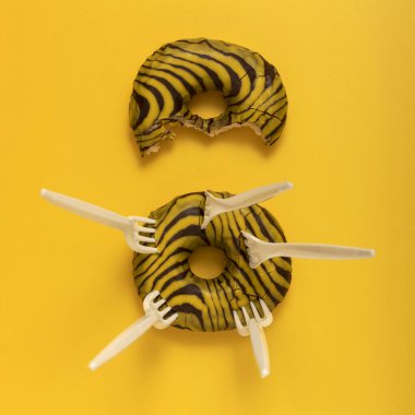 Donuts and disposable plastic forks on a yellow background. Top view.