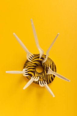 Donut and disposable plastic forks on a yellow background.