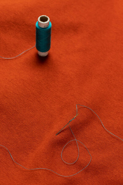 A needle with blue thread on orange fabric. Close-up.