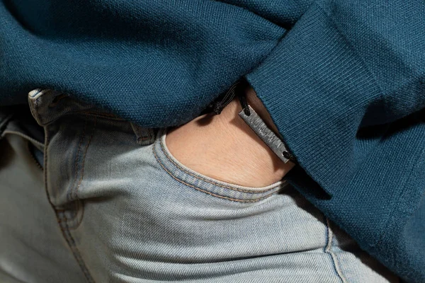 Unrecognizable person in jeans and an oversized blue sweater. Extreme close-up.