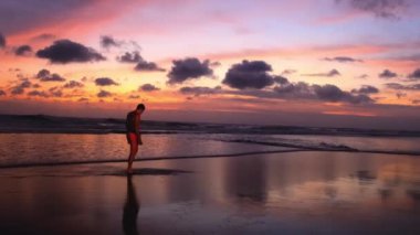 Okyanusta yürüyen bir adamın tam boy silueti. Parlak, ateşli, çok renkli günbatımına karşı. Dalgaların huzur ve sesinin tadını çıkaran bir adam. Güzel bir manzaranın yavaş çekim 4k görüntüsü