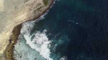 Yeşillikle kaplı bir okyanus kayalığının yukarıdan görünen görüntüsü. Endonezya 'nın Nusa Penida adasında bulutlu bir günde turkuazlı berrak su dalgaları. Seyahat konsepti. Drone görünümü