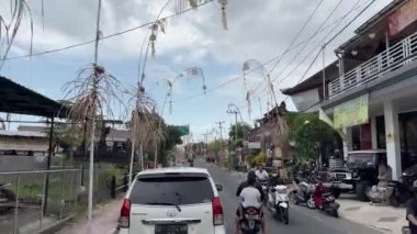 Yol boyunca Penjor. Hareket halindeki bir araçtan yola bak. Kamera arabayı takip ediyor. Yolda bir sürü bisiklet var. Asya. Bali, Endonezya, 4 Eylül 2022