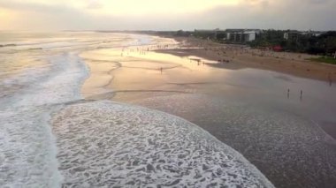 İnsansız hava aracı görüntüleri bir okyanus sahilinde uçuyor ve Endonezya 'daki Bali adasında gün batımını izleyen bir kalabalık var. Seyahat ve doğa. 4k