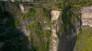 Yeşil ile kaplı okyanus kayalıklarının yukarıdan görünen manzarası. Endonezya 'nın Nusa Penida adasında bulutlu bir günde, turkuazlı berrak su dalgaları kıyıya hücum eder. Seyahat kavramı. İnsansız hava aracı görüntüleri