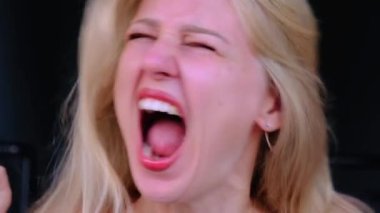 Sarışın bir kadının ağzı açık bağırıp kafasını salladığı yakın plan bir fotoğraf. Zor duygusal durumdaki bir kadın. Histeri, zihinsel sorunlar. Öfke, korku, acı. Aşırı duygu bolluğu.