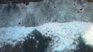 Okyanus sörfünün hava görüntüsü. Kalın beyaz köpüklü büyük mavi dalgalar kıyıları kaplıyor. Kuş bakışı ateş edilmiş. Nusa Penida Adası, Endonezya. Doğanın gücü ve gücü.