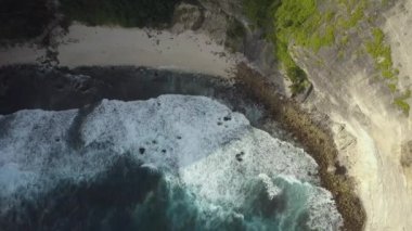Uçağı, cennet adası Nusa Penida 'daki kayalık uçurumdan uçuyor. Dalgalar kayalara çarpar. Su zümrüttür, koyu mavi ve yeşil. Güzel turkuaz Hint Okyanusu manzarası.