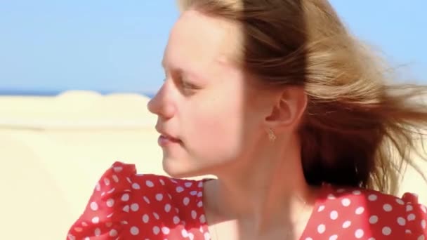 若い女の子は青い空に太陽の下で目を細めている 白人の女の子は孤独を楽しんで 風が彼女の髪をフリルしながら距離を調べる 一人時間だ 女性のクローズアップ肖像画 — ストック動画