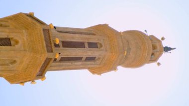 Minaret of the mosque. Vertical 4k close-up video view from below on a high minaret against a blue clear sky and the sun.