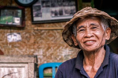 Horizontal portrait of a South Asian Senior Men wearing a traditional Balinese cone hat. Elderly man looking at the camera smiling.