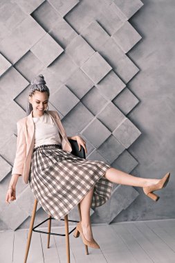 Çekici, neşeli iş kadını kafasında Rasta ile gri bir arka planda bir sandalyeye oturuyor..