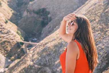 Genç çekici esmer, dağların arka planında oturup güneşin tadını çıkarıyor. Seyahat, yürüyüş, boş zaman ve tatil konsepti