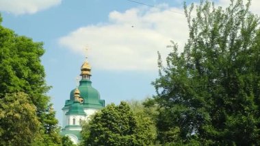Yeşil çatılı ve altın kubbeli Ortodoks kilisesi güneşli bir yaz gününde ağaçların arkasından mavi bir gökyüzüne bakıyor. Ukrayna 'da sıradan bir kilise
