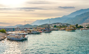 Kas, Antalya, Turkey - August 7, 2024: Daily boat tours anchored at the seaside and waiting for passengers. Kas harbour and kas city and mountain in the background. clipart