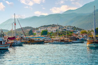Kas, Antalya, Türkiye - 7 Ağustos 2024: Deniz kenarında demirlemiş ve yolcu bekleyen günlük tekne turları. Kas limanı ve Kas şehri ve arka planda dağ.