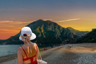 Rear view, back view of a woman walking along the seashore towards Olympos at sunset. Antalya, Turkey. clipart