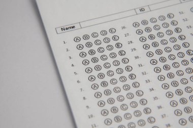 Mavi bir kalemi tutan bir eli gösteriyor ve bir sınav kağıdına 