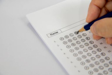 Mavi bir kalemi tutan bir eli gösteriyor ve bir sınav kağıdına 