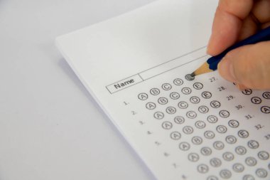 Mavi bir kalemi tutan bir eli gösteriyor ve bir sınav kağıdına 