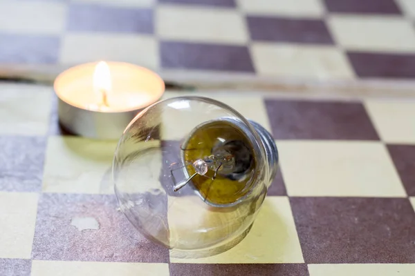 stock image Burning candle and lamp on a chessboard. Blackout due to war in Ukraine