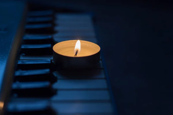 A burning candle on the keys of the synthesizer near the sheets with notes. Blackout in Ukraine due to war