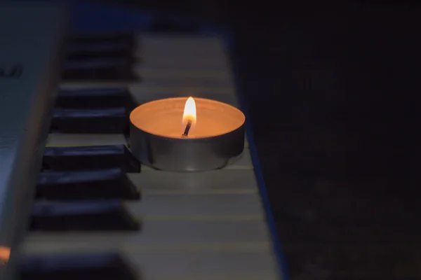 A burning candle on the keys of the synthesizer near the sheets with notes. Blackout in Ukraine due to war