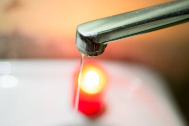 Yanan bir mumun arka planına karşı musluktan gelen ince bir su püskürtüsü. Savaş nedeniyle Ukrayna 'da elektrik ve su kesintileri